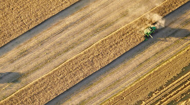 Flygfoto över åker med traktor som skördar