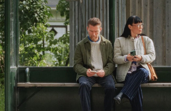 En man och en kvinna sitter i en busskur med sina telefoner i handen