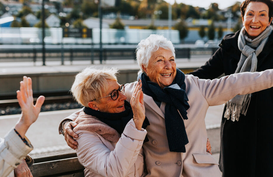 En grupp glada äldre kvinnor sitter på en bänk och skrattar tillsammans