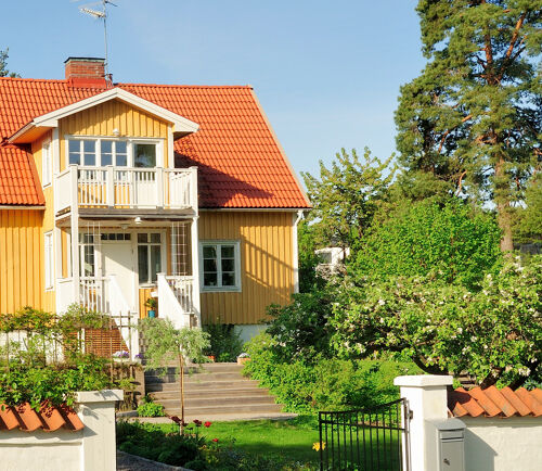 Gult hus med vit veranda och grönskande trädgård utanför Stockholm