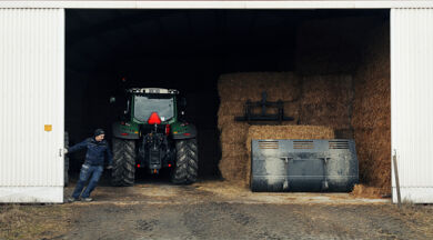 Traktor och höbalar innanför öppen ladugårdsdörr