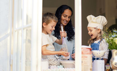 Vuxen och två barn syns genom fönster, bakar i kök