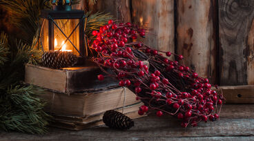 Krans med röda bär ligger på ett bord intill några böcker och en ljuslykta