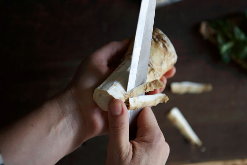 Närbild på händer som skalar en pepparrot med en kniv.