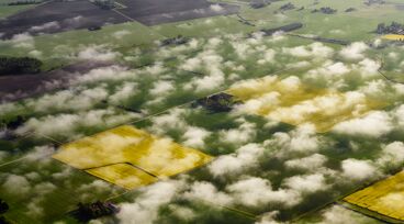 Flygfoto över åker med moln i förgrunden